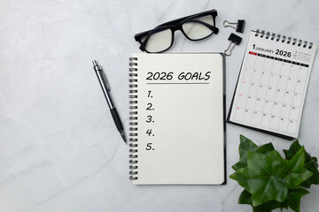 Spiral notebook titled 2026 Goals on a white marble desk with pen, glasses, calendar and green plant, symbolizing New Year goal planning, strategy roadmap, productivity habits and fresh beginnings.