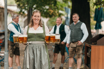 Happy woman waitress in dirndl serving big beer mugs to friends