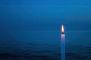 A single white candle flame flickers against a deep blue twilight sea