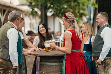 Happy woman waitress in Bavarian costume serving large mugs of beer to friends enjoying Oktoberfest celebration friendship and tradition