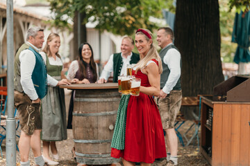 Traditional waitress serves beer mugs to group of Bavarian friends celebrating Oktoberfest in beer garden enjoying friendship leisure and culture