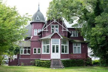 Historic red wooden villa with tower and large windows surrounded by trees