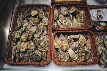 Baskets of fresh unopened oysters on crushed ice at a seafood market, neatly displayed for sale as a raw gourmet delicacy, ideal for restaurants, catering or retail purchase