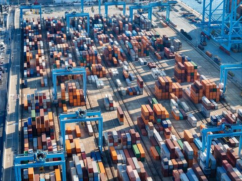 Vado Gateway, Italy - 21 September 2025: Aerial view of stacked shipping containers creating a vibrant tapestry of colors at the bustling port, contrasted by the cool blue of the cranes.