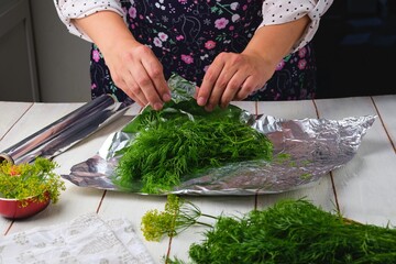 Step-by-step preparation of frozen dill in a foil wrapper for freezer storage on a light wooden background.