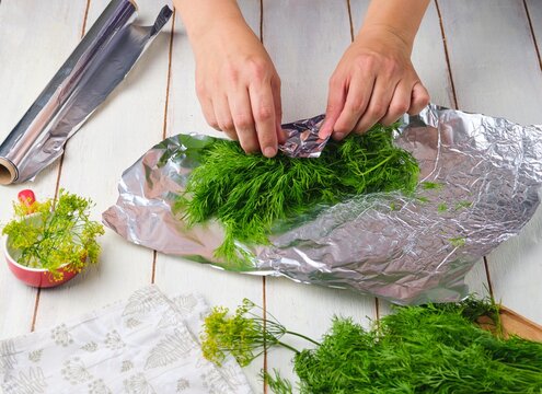 Step-by-step preparation of frozen dill in a foil wrapper for freezer storage on a light wooden background.
