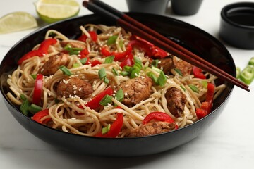 Tasty noodles with chicken, green onions and vegetables served on white table, closeup
