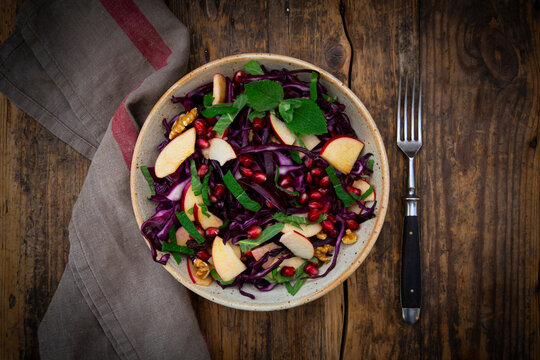 Autumnal salad with red cabbage apple pomegranate mint and walnut on wood