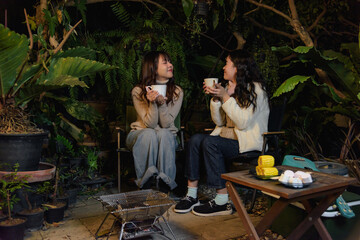 Winter camp outdoor, happy women friends in forest enjoy warm drinks, people share cozy moments on chilly winter evening, barbecue grill adds to outdoor fun