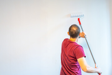 Man painting the wall with an extended roller during home renovation to reach higher surfaces. Concept of efficient interior work, broad coverage and advanced DIY improvement.