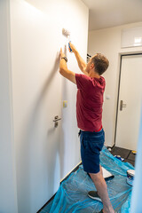 Man painting the wall with a roller in white during home renovation. Interior improvement, surface transformation and DIY work with paint tools.