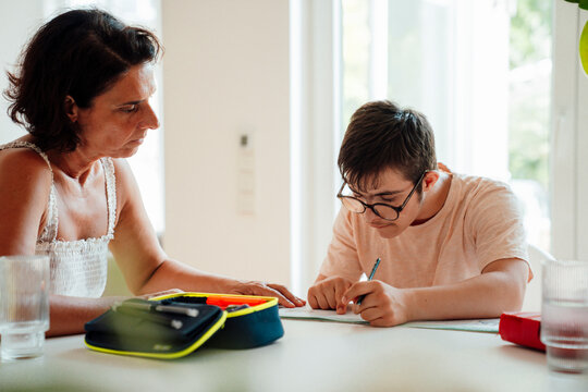 Mother supporting son with trisomy 21 doing homework indoors