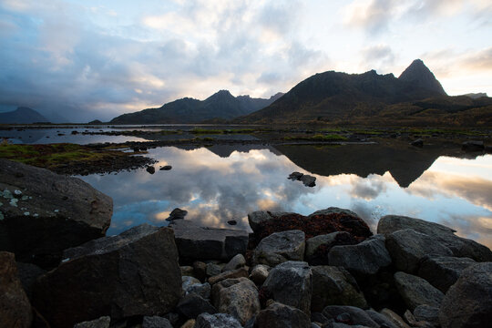 Moody dusk over the mountains near Klo, Vester&aring;len, Norway. Jagged peaks cast reflections in still tidal pools, framed by rugged rocks and a dramatic Arctic sky.