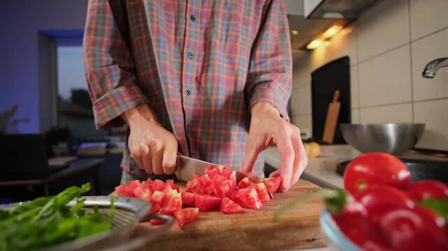 Close up of male hands slicing fresh tomatoes for salad on wooden board in authentic kitchen evening lifestyle atmosphere healthy eating scene.