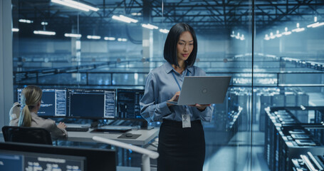 Asian Female Information Technology Engineer Reviews Security Logs on Her Laptop Computer in a High-Tech Data Center, Analyzing Potential Risks to Ensure Network’s Safety and Compute Power