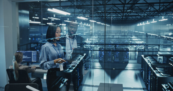 In a Modern Data Center, Black Male Data Scientist and Asian Female AI Specialist Analyze Algorithms on a Laptop. Specialists Exploring Optimizations for Processing Large Datasets
