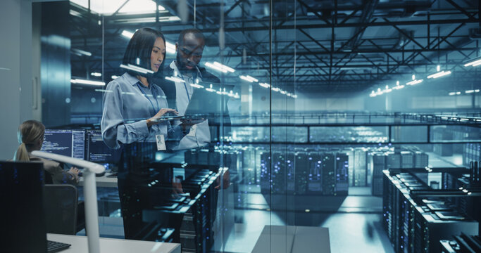 African Male Cloud Security Engineer and Asian Female IT Manager Work Side by Side on a Laptop in a Data Center, Conducting a Thorough Security Audit of the Server Network Infrastructure