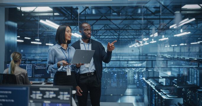 In a Modern Data Center, Black Male Data Scientist and Asian Female AI Specialist Analyze Algorithms on a Laptop. Specialists Exploring Optimizations for Processing Large Datasets - Powered by Adobe