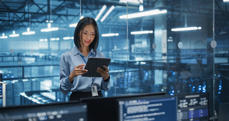 Asian Female Systems Administrator Standing in a Glass Office, Adjusting Configuration Settings on Her Tablet Computer, Operating Cloud Services Servers for Artificial Intelligence Training
