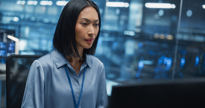 Portrait of a Asian Female Data Center Specialist Analyzing System Performance on a Laptop, Optimizing Cybersecurity Protocols in a High-tech Facility. Developer Monitors Real-time Data on Computer - Powered by Adobe