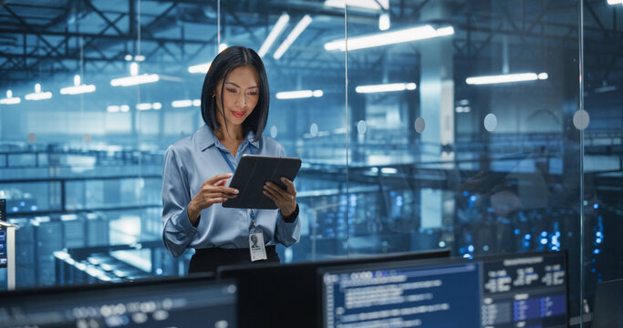 Asian Female Systems Administrator Standing in a Glass Office, Adjusting Configuration Settings on Her Tablet Computer, Operating Cloud Services Servers for Artificial Intelligence Training