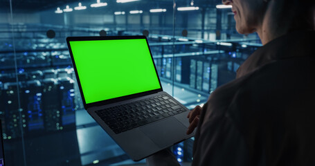 Portrait of a Female Systems Administrator Standing in a Glass Office, Adjusting Configuration Settings on Her Laptop Computer with Green Screen Template for Screen Replacement