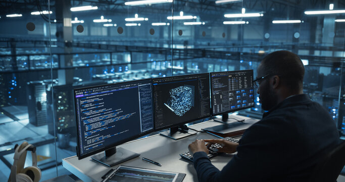 Male Software Engineer Focused on Working on a Machine Learning Model Displayed Across Three Monitors. Black Specialist Analyzing Data Outputs and Tweaking Parameters in Real Time