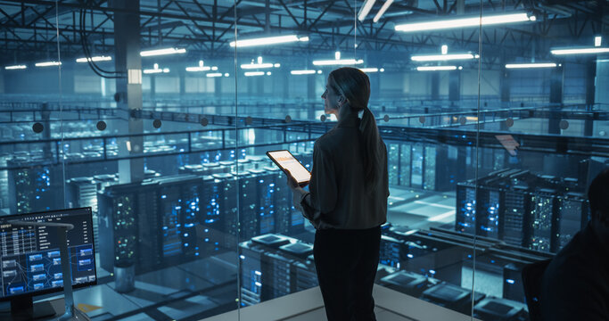 Female Information Technology Engineer Reviews Security Logs on Her Tablet Computer in a High-Tech Data Center, Analyzing Potential Risks to Ensure Network’s Safety and Compute Power