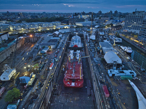 Brooklyn, United States - 13 August 2023: Aerial view of the Brooklyn Navy Yard, where massive ships rest in dry docks under the fading light of dusk.