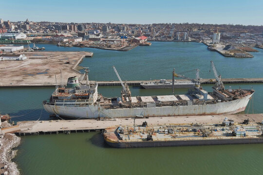 Brooklyn, United States - 11 February 2022: Aerial view of the rusting hulk of a cargo ship moored beside the pier, a stark contrast against the glistening water and the industrial landscape.