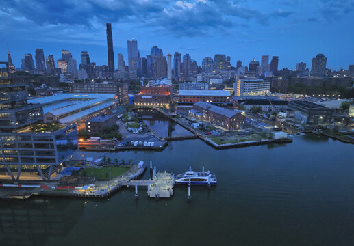 Brooklyn, United States - 13 August 2023: Aerial view of the skyline fading into the deep blue dusk, the East River reflecting the city's twinkling lights near the Brooklyn Navy Yard.
