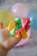 hand holding colorful deflated balloons with blurred inflated balloons in background, festive and playful party preparation concept
