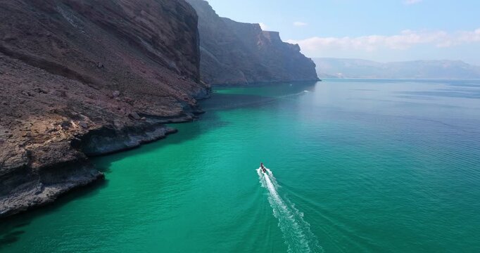 Boat Cruising On Tranquil Shores With Dramatic Cliffs In Shoab Beach, Socotra Island, Yemen. Aerial Drone Orbit Shot