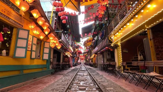 Hanoi Train Street decorated with colorful lanterns and lights, with railway tracks running through lively cafes on both sides in the morning..