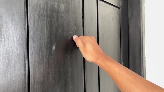 View of a hand knocking on a black door