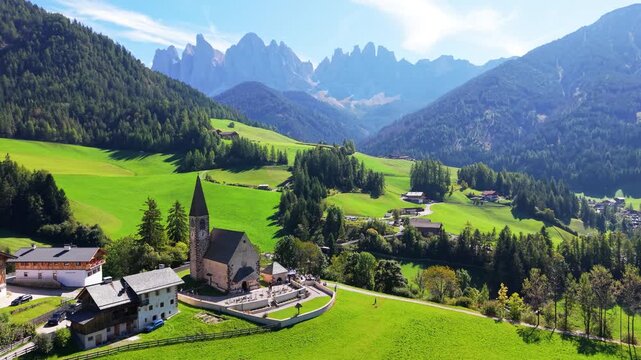 Aerial Drone Footage flying over to Santa Maddalena Church and Odle Dolomites, Val di Funes, South Tyrol, Italy ,captures the small alpine village surrounded by green meadows, farmhouses.