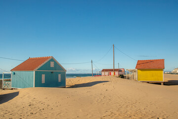 Caparica, Lisbon, Portugal. 2 December 2023. Beach huts with red and yellow facades on sand dunes by the Atlantic coast