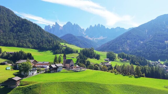 Aerial Drone Footage flying over to Santa Maddalena Church and Odle Dolomites, Val di Funes, South Tyrol, Italy ,captures the small alpine village surrounded by green meadows, farmhouses.