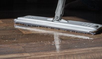 Close-up of a mop cleaning a wooden floor with water and detergent