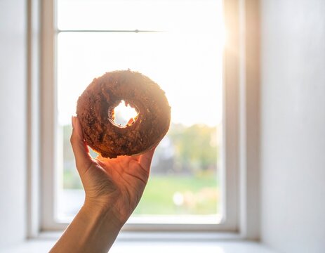 Hand Holding an Doughnut Against a Sunny Window with Golden Afternoon Light
. 