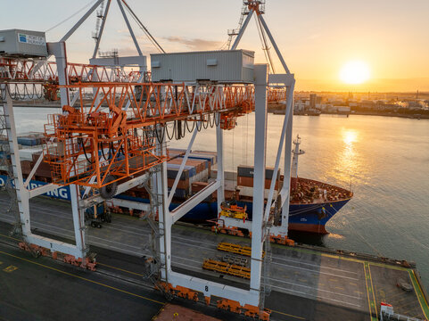 Tauranga, New Zealand - 24 February 2025: Aerial view of container ship dwarfed by towering cranes, bathed in the warm glow of the setting sun at Mirrielees Road.