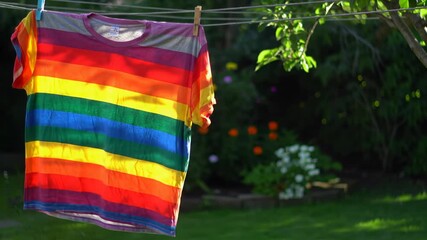 Rainbow striped t-shirt hanging on a clothesline in a sunny garden. Symbolizes PRIDE month and inclusivity, promoting diversity.