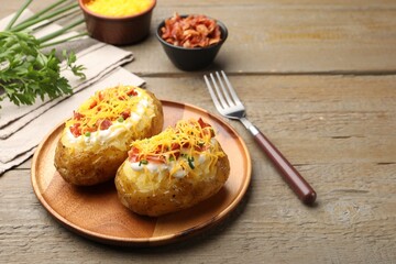 Tasty baked potatoes with sour cream, green onion, cheese and bacon served on wooden table, closeup