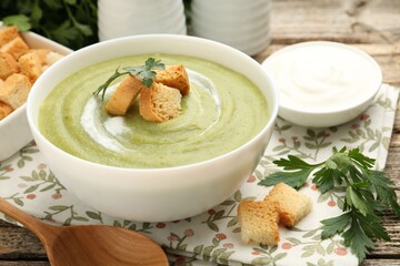 Tasty broccoli cream soup with croutons served on wooden table, closeup