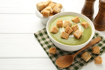 Tasty broccoli cream soup with croutons served on white wooden table, closeup. Space for text