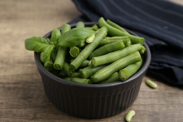 Pieces of fresh green beans and basil leaves in bowl on wooden table, closeup