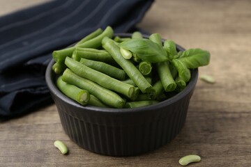 Pieces of fresh green beans and basil leaves in bowl on wooden table, closeup