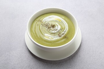 Tasty broccoli cream soup on light grey table, closeup