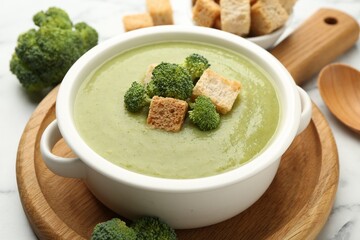 Tasty broccoli cream soup with croutons served on white marble table, closeup