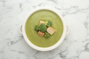 Tasty broccoli cream soup with croutons on white marble table, top view